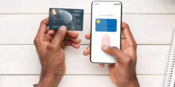 Image Depicting Biometric App Usage: two hands holding a phone and a bank card, using a fingerprint ID to log in